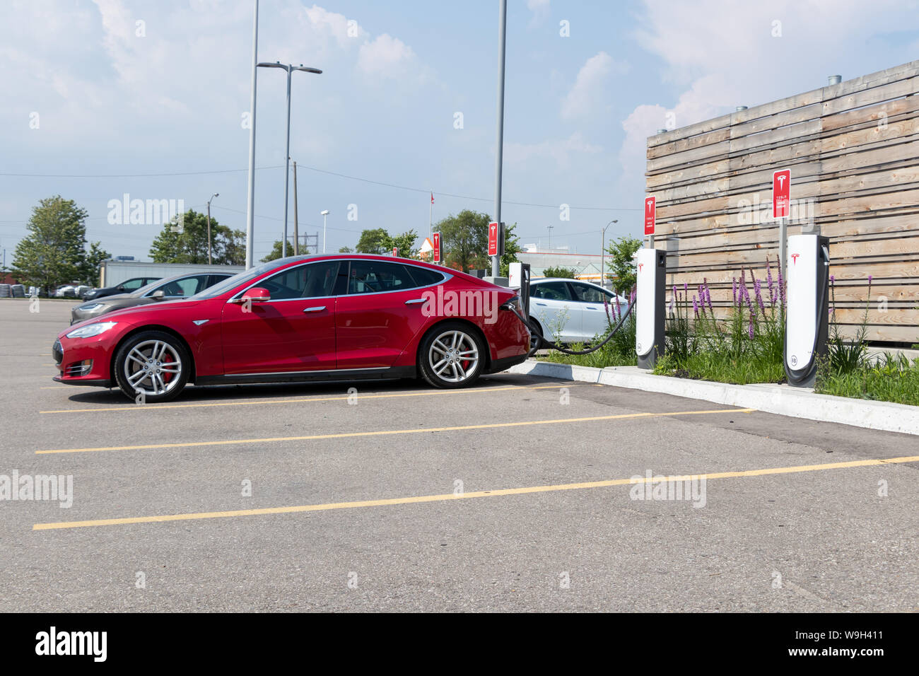 Tesla Model S rouge branché en charge, à l'Urbain Tesla Supercharger avec Modèle X et de la Model S en arrière-plan. Banque D'Images