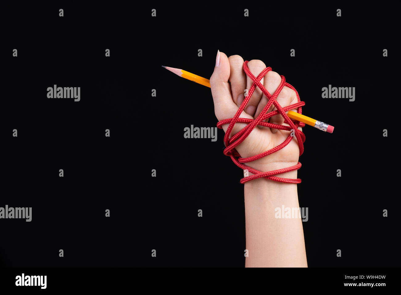 Femme la main avec un crayon jaune attaché avec la corde rouge, illustrant l'idée de la liberté de la presse ou d'expression sur fond sombre. Journée mondiale de la liberté de la presse et Banque D'Images