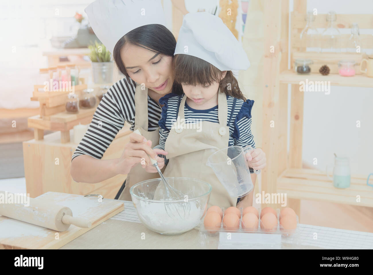 Famille heureuse dans la cuisine. Mère et sa fille asiatique préparer la pâte pour faire un gâteau. Banque D'Images