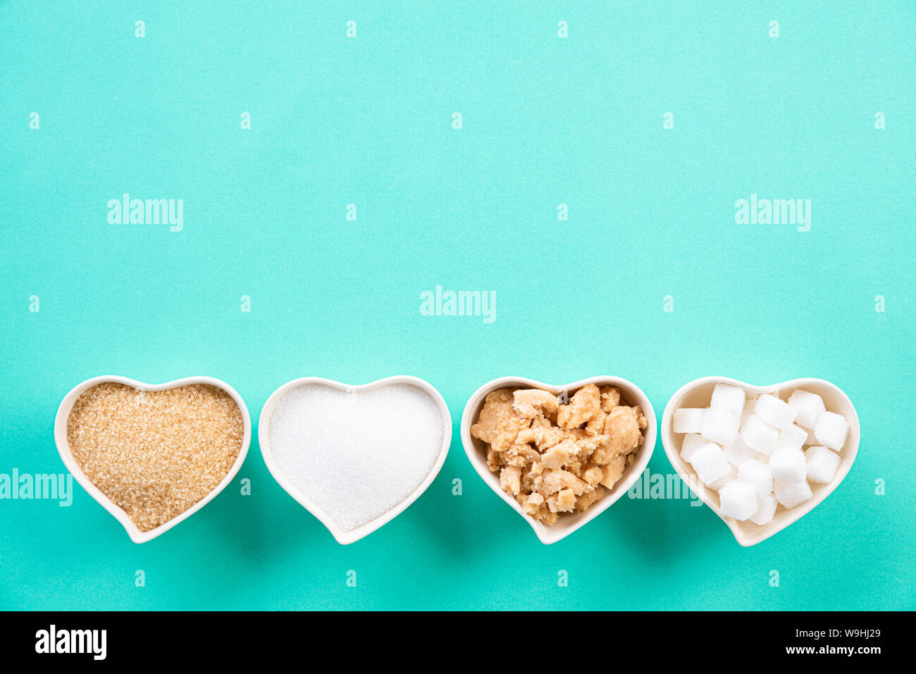 Vue de dessus de différents types de sucre. Cube, sucre brut le sucre brun et le sucre granulé dans coeur bol vert clair sur fond pastel. Mise à plat. Banque D'Images