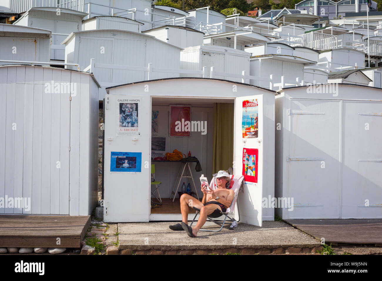 Un homme est assis dans sa chaise longue la lecture d'un livre à l'extérieur de sa cabane de plage sur le front de mer de Sainte Adresse, Le Havre, Normandie, France Banque D'Images