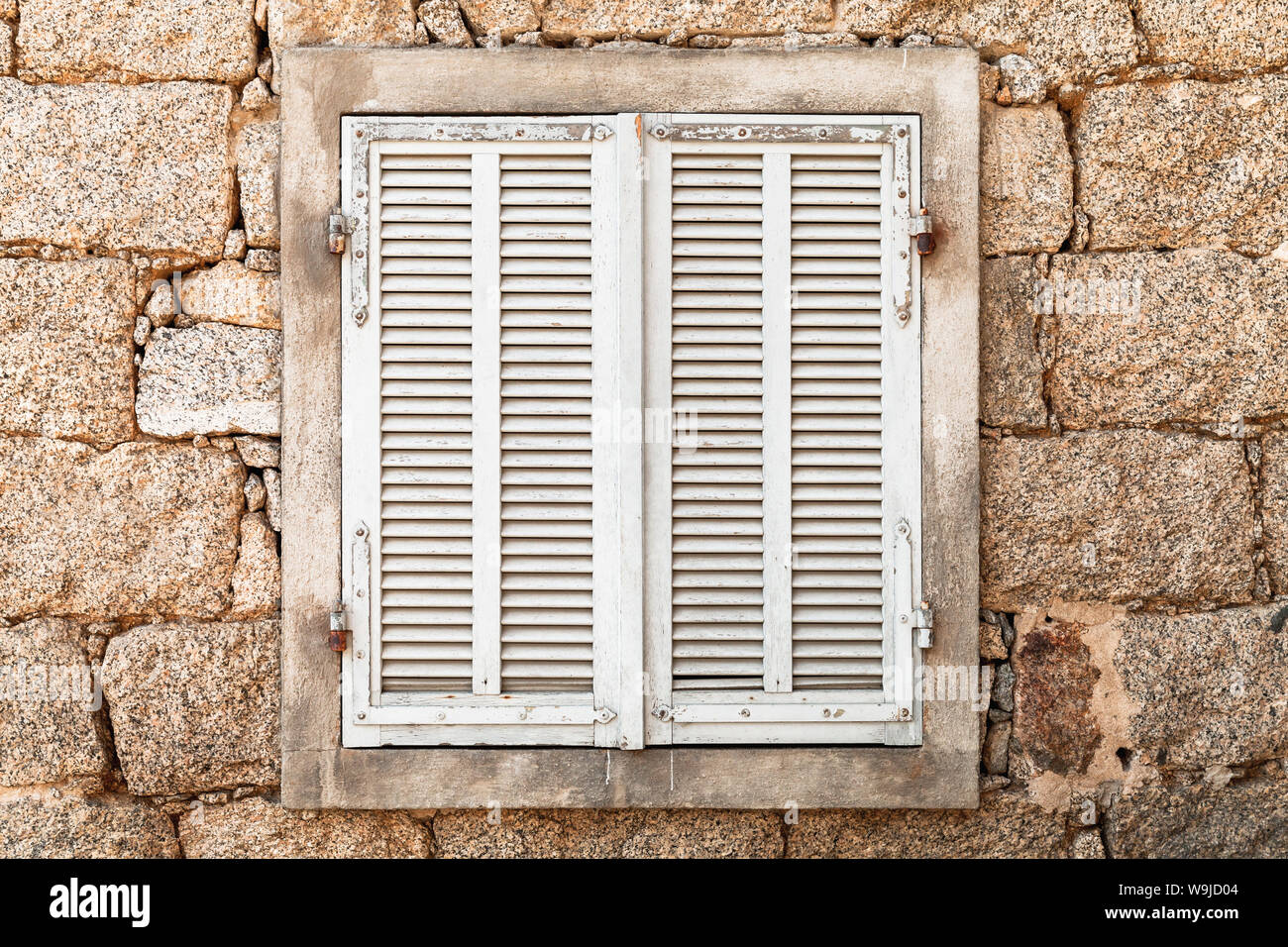 Vieille fenêtre fermée avec volets en bois blanc dans l'ancien mur de pierre, vue de face, la texture de fond photo Banque D'Images