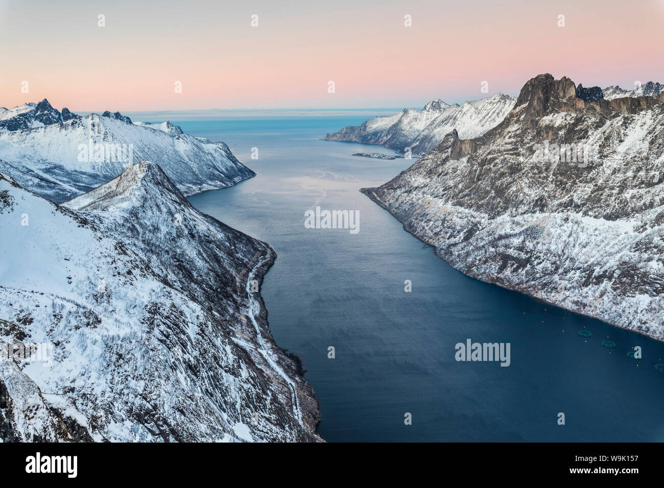 Vue de dessus les cimes enneigées entourant Fjordgard encadrée par la mer gelée au coucher du soleil, Ornfjorden, Senja, Troms, Norway, Scandinavia, Europe Banque D'Images