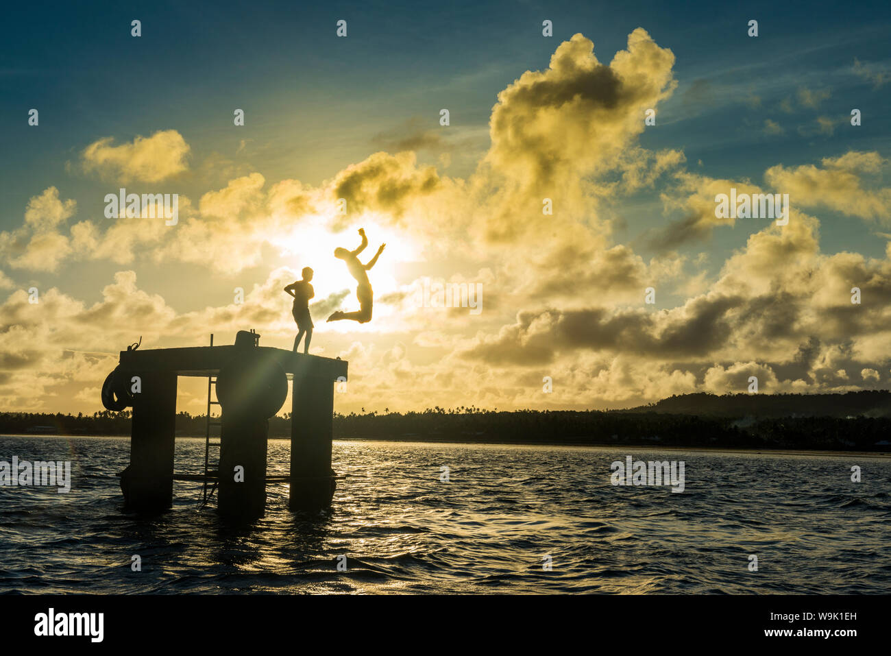 Les garçons local rétroéclairé sautant dans l'eau du lagon de Wallis à partir d'une plate-forme, Wallis et Futuna, Pacific Banque D'Images
