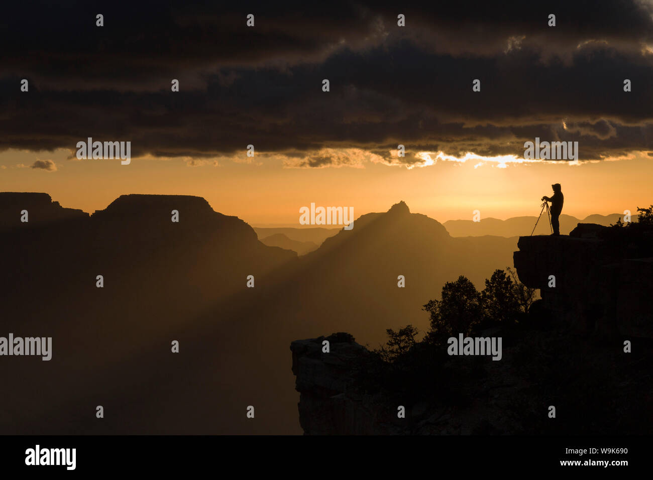Un photographe solitaire se tient perché sur un rocher qui se profile contre l'aube ciel orange à Yaki Point, Grand Canyon National Park, l'UNESCO, Arizona, USA Banque D'Images
