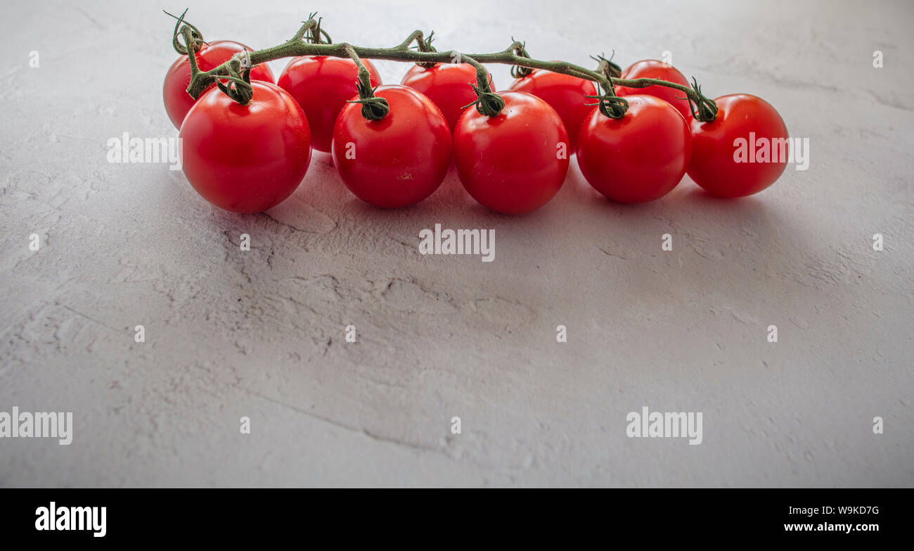 La photographie culinaire - vue latérale des petites tomates cerises rouges sur la vigne sur un fond texturé blanc ordinaire Banque D'Images