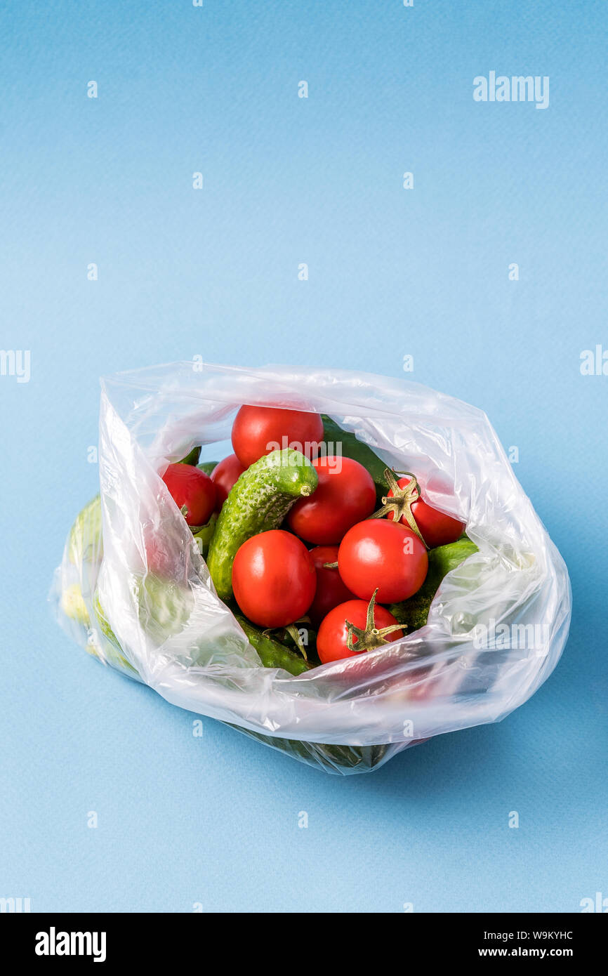 Vue de face des concombres et des tomates dans un sac plastique sur fond bleu. Image montre le harmness à l'aide de sacs de stockage de l'alimentation artificielle. La verticale. Banque D'Images