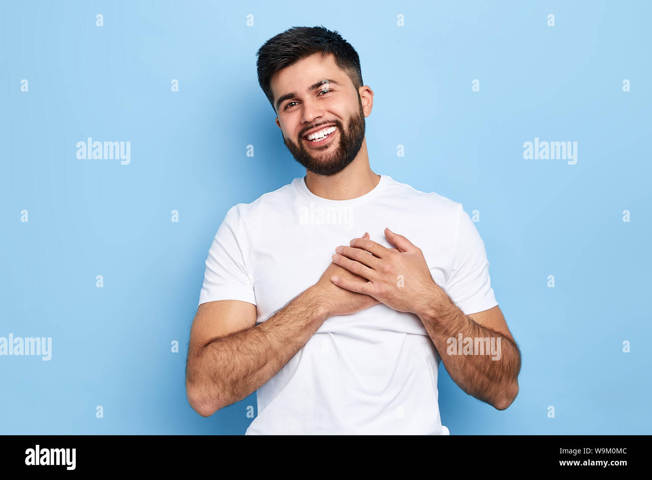 Heureux heureux hipster guy sourit joyeusement, garde les mains sur le cœur, exprime des émotions agréables sympathie et beaucoup d'amour.portrait, l'homme a falle Banque D'Images