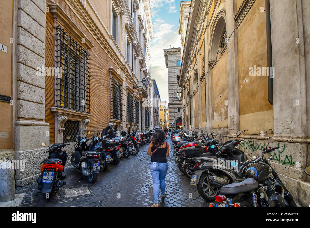 Une femme marche seul dans une petite rue latérale, avec beaucoup de motos en stationnement sur un côté ou dans le centre historique de Rome, Italie Banque D'Images