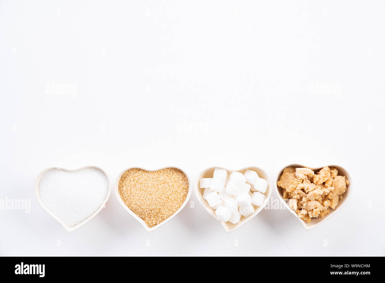 Vue de dessus de différents types de sucre. Cube, sucre brut le sucre brun et le sucre granulé dans coeur bol sur fond blanc. Mise à plat. Banque D'Images