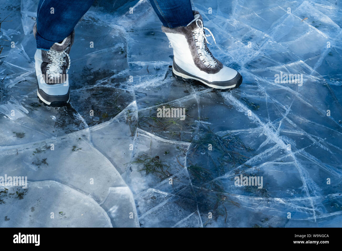 Les femmes en bottes blanches marche sur glace craquelée bleu Banque D'Images