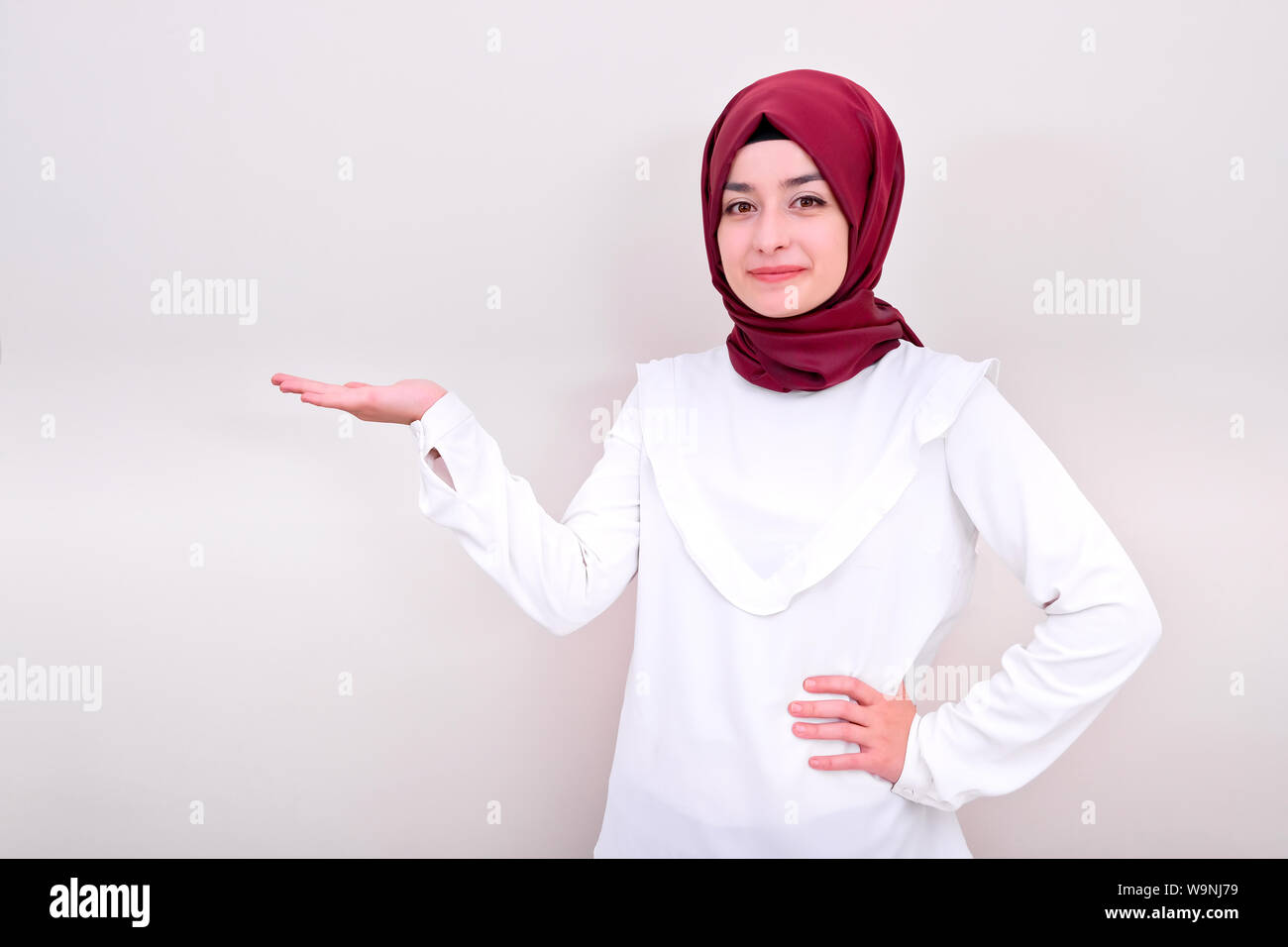 Femme musulmane tenue exemplaire en blanc l'espace à sa main ouverte, paume hijab fille à l'appareil photo, le fond est blanc isolé Banque D'Images