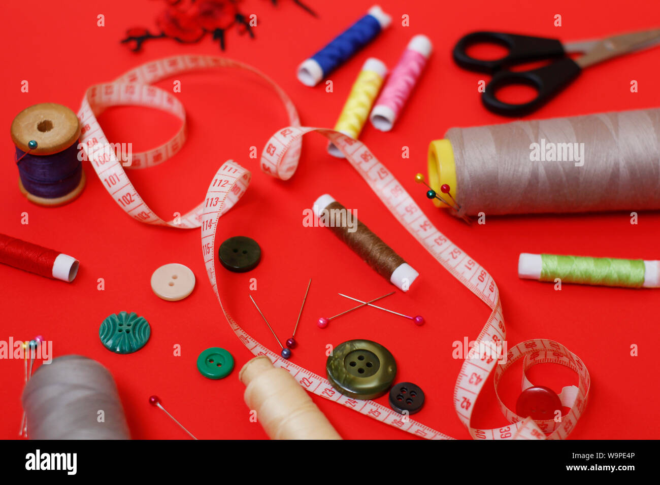 La composition avec filets et accessoires de couture sur un fond rouge. Fournitures et accessoires pour les travaux d'aiguille à coudre. Des bobines de fil, des ciseaux et l'aiguille Banque D'Images