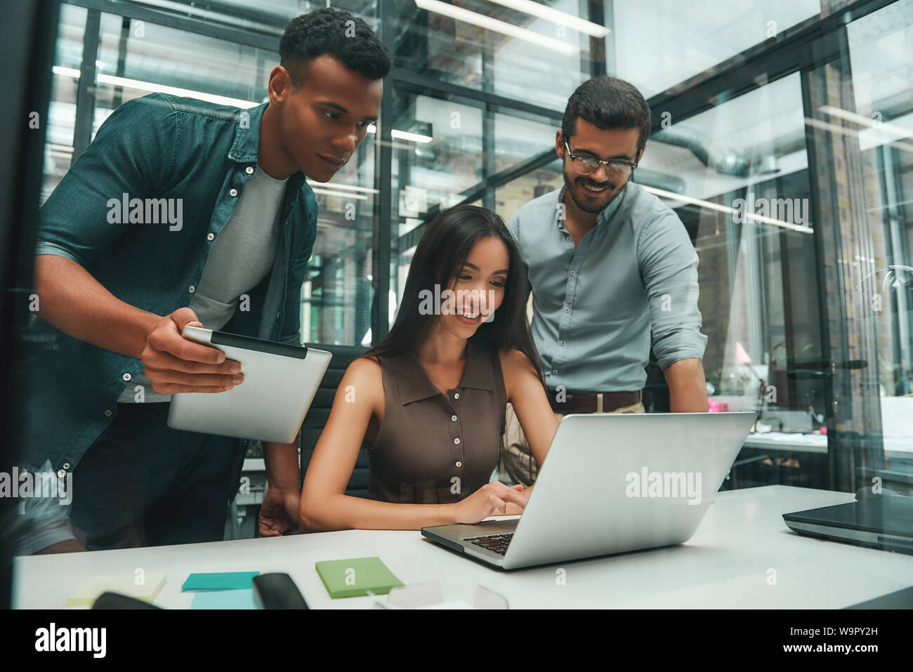 Les gens d'affaires. Groupe de trois jeunes et joyeux employés utilisant les technologies modernes tout en travaillant dans un bureau moderne. Concept d'emploi. Lieu de travail Banque D'Images