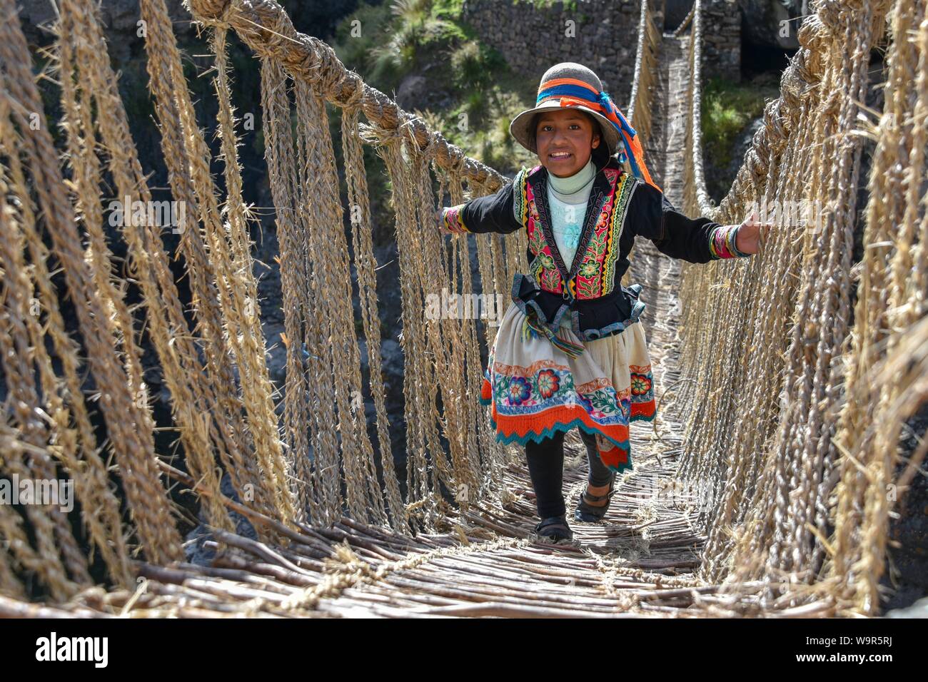 Rire fille locaux en costume traditionnel passant sur le pont suspendu de Inca Q'iswachaka, pont de corde tressée de Ichu grass sur la rivière Banque D'Images