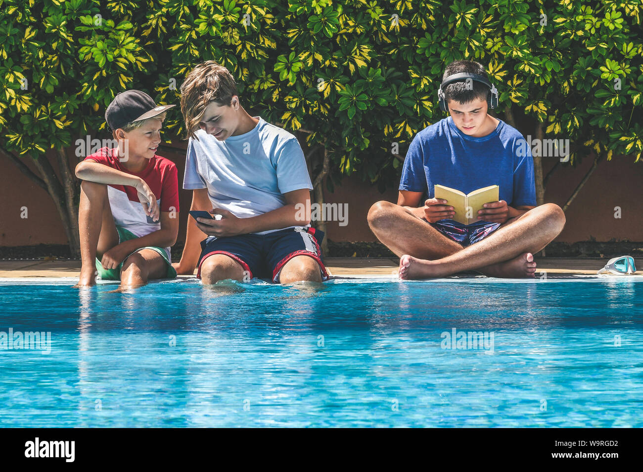 Jeune homme profitant de jours de congé de l'école de vous détendre dans la piscine. Livre de lecture, l'écoute des adolescents la musique et regarder des vidéos en ligne avec smartpho Banque D'Images