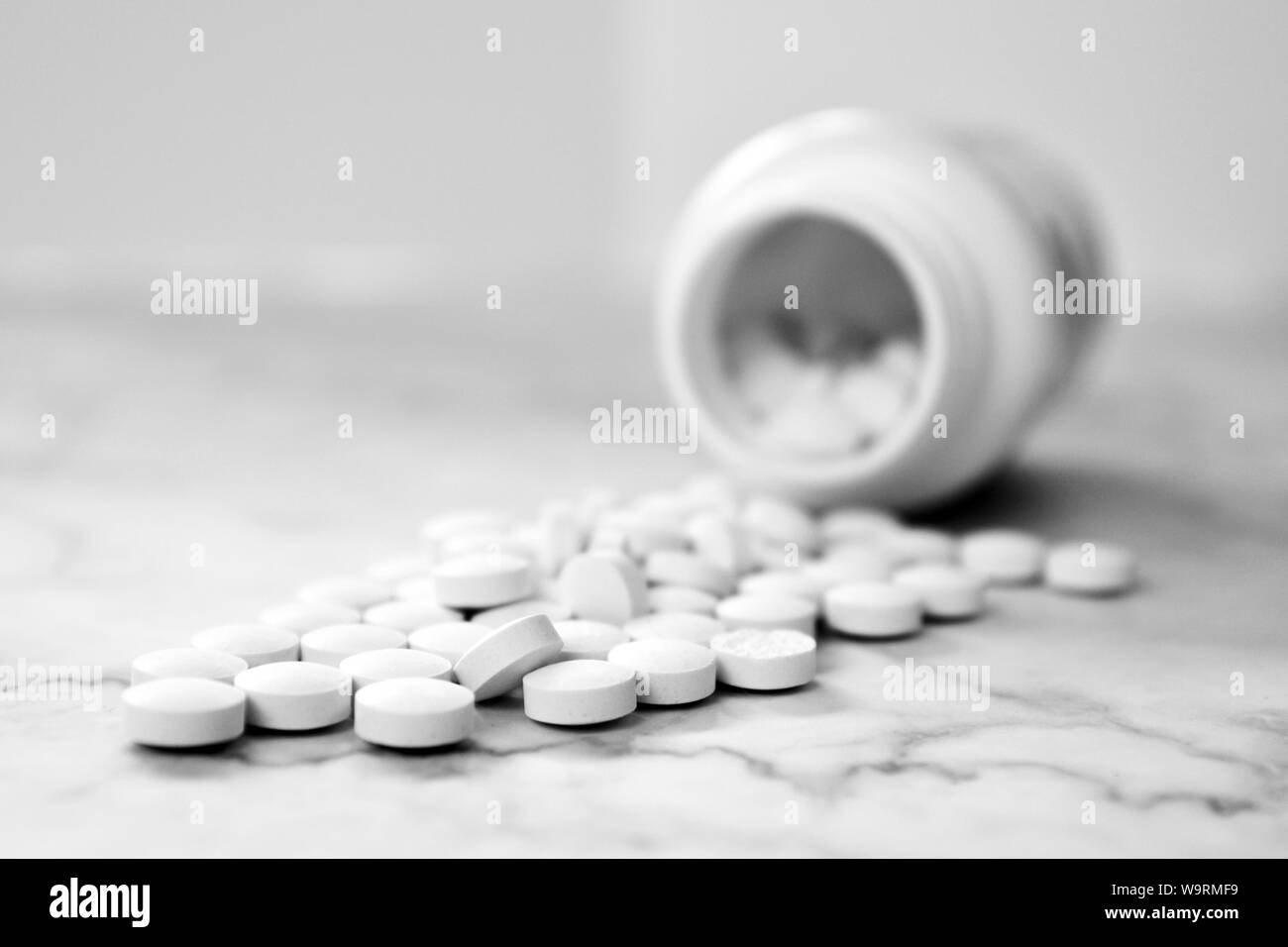 Beaucoup de pilules médical blanc déversant à partir d'un récipient en plastique flacon de médicaments sur fond clair Banque D'Images