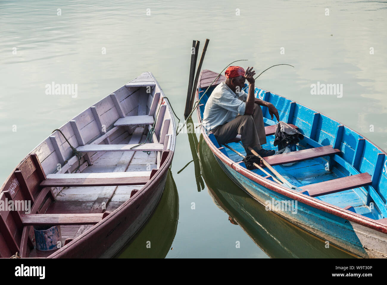 Vieil homme assis dans un bateau de pêche en bois tout en fumant une cigarette Banque D'Images