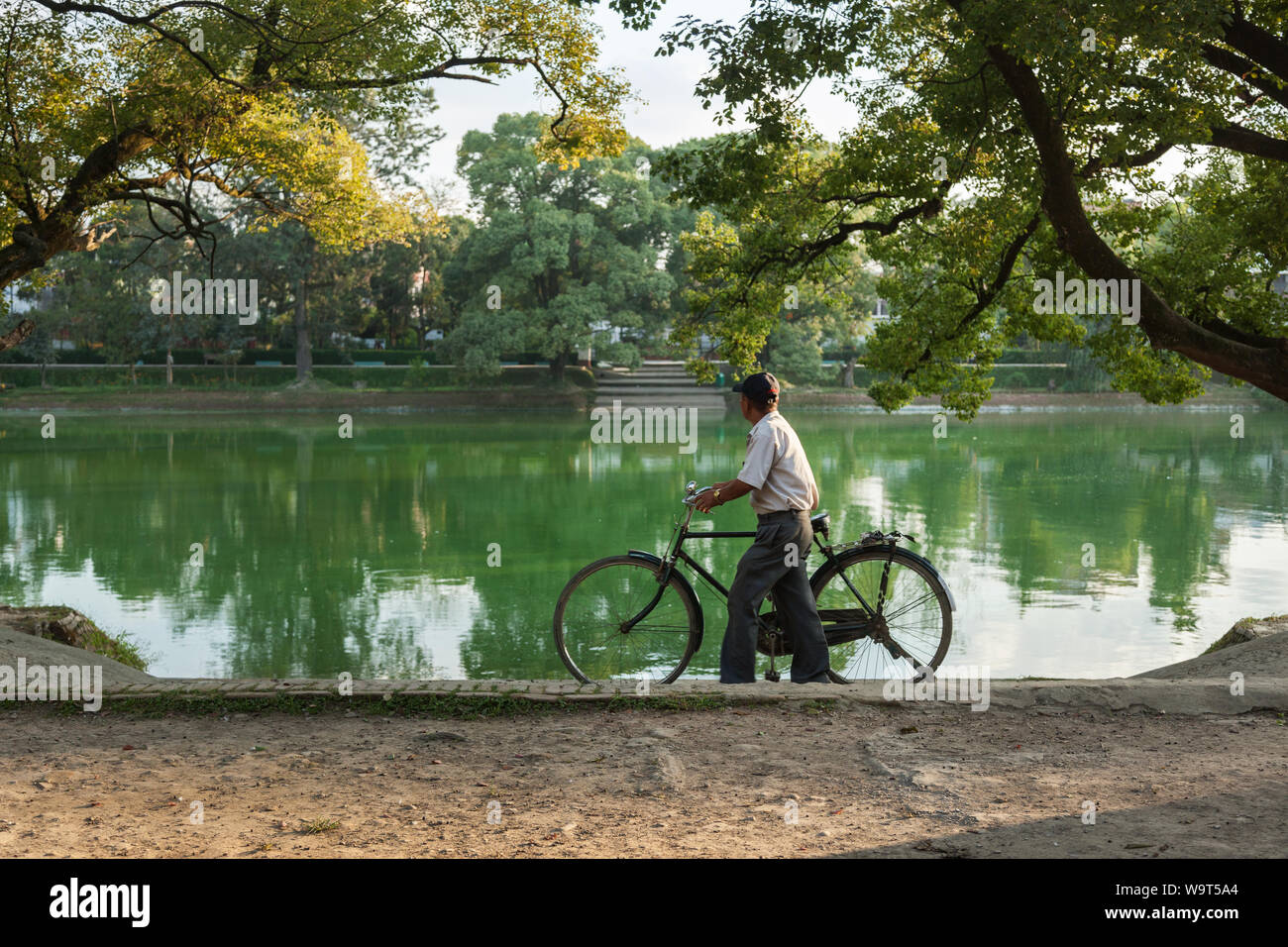 Homme marchant avec son vélo dans un parc à côté d'un lac. Banque D'Images