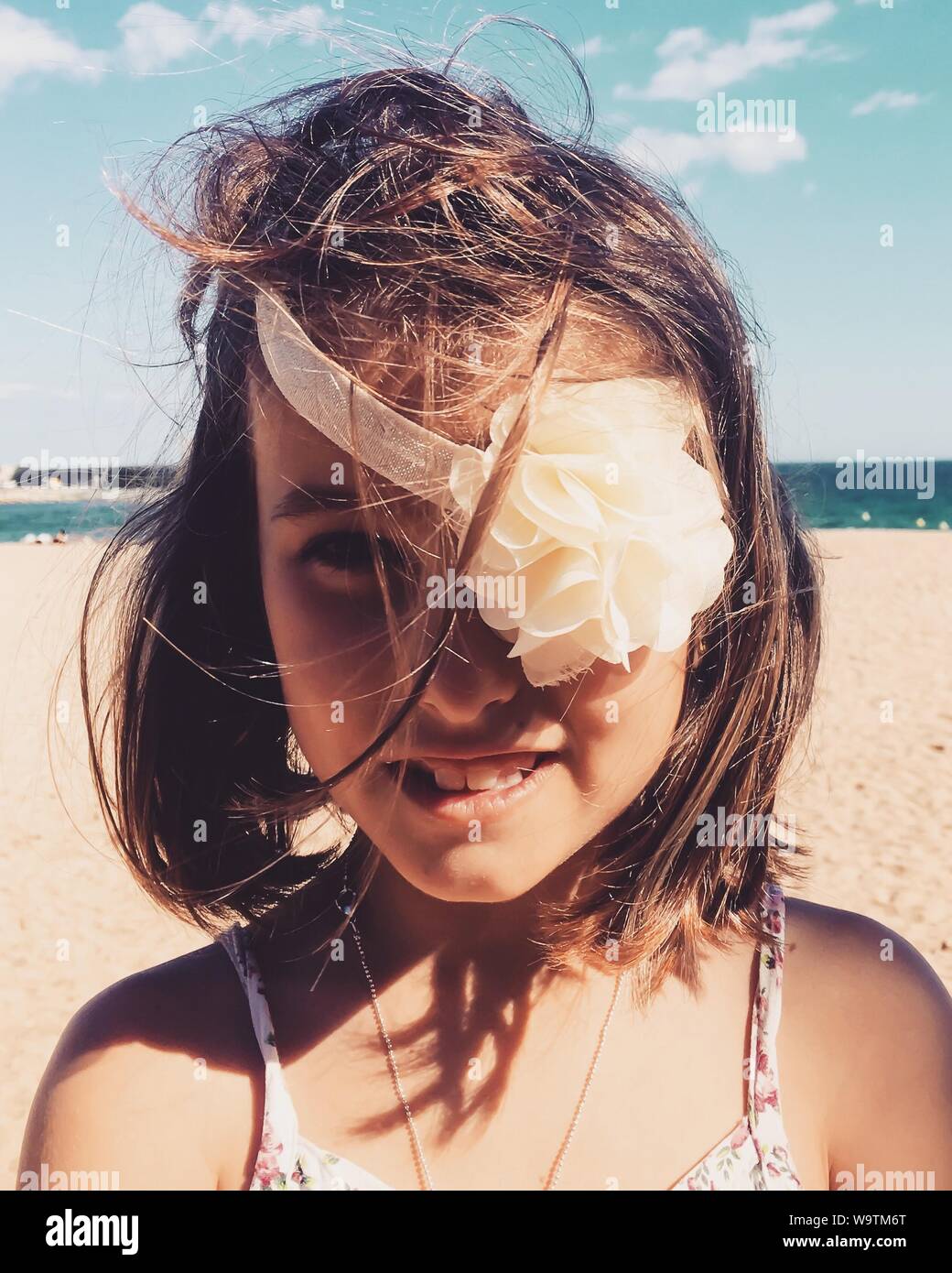 Portrait of a smiling girl sur la plage avec un serre-tête floral couvrant son œil, Espagne Banque D'Images
