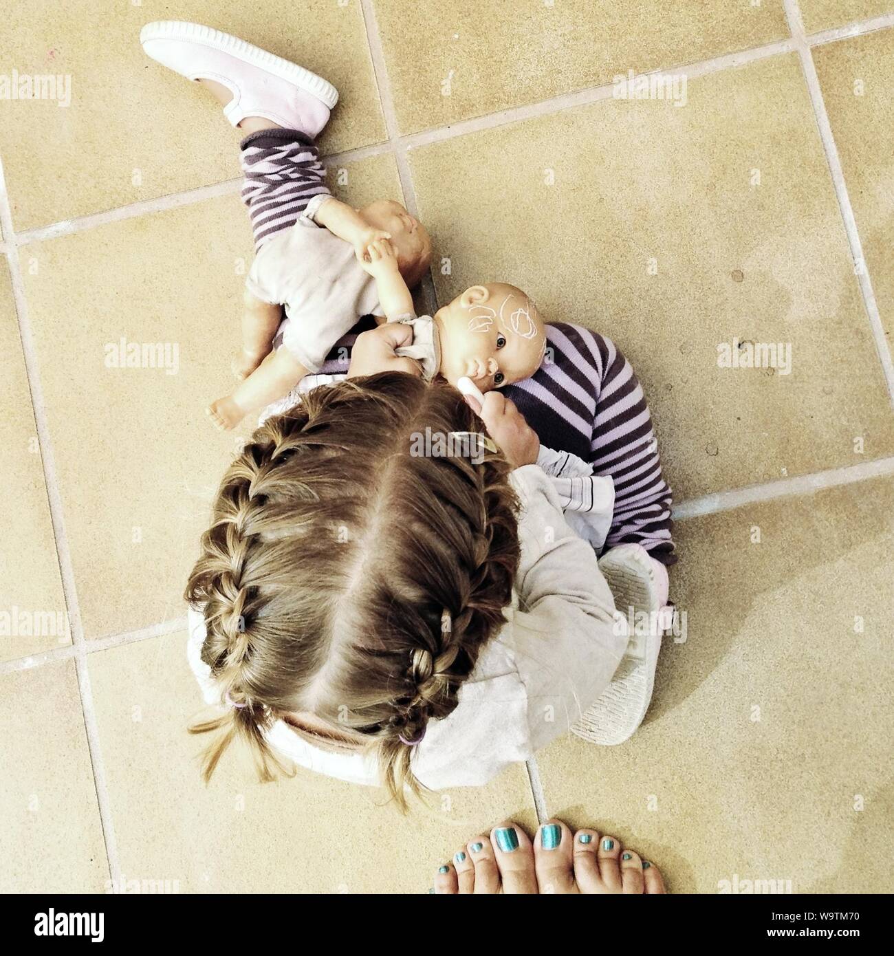 Vue aérienne d'une femme de pieds à côté d'une fille assise sur le sol à jouer avec des poupées Banque D'Images