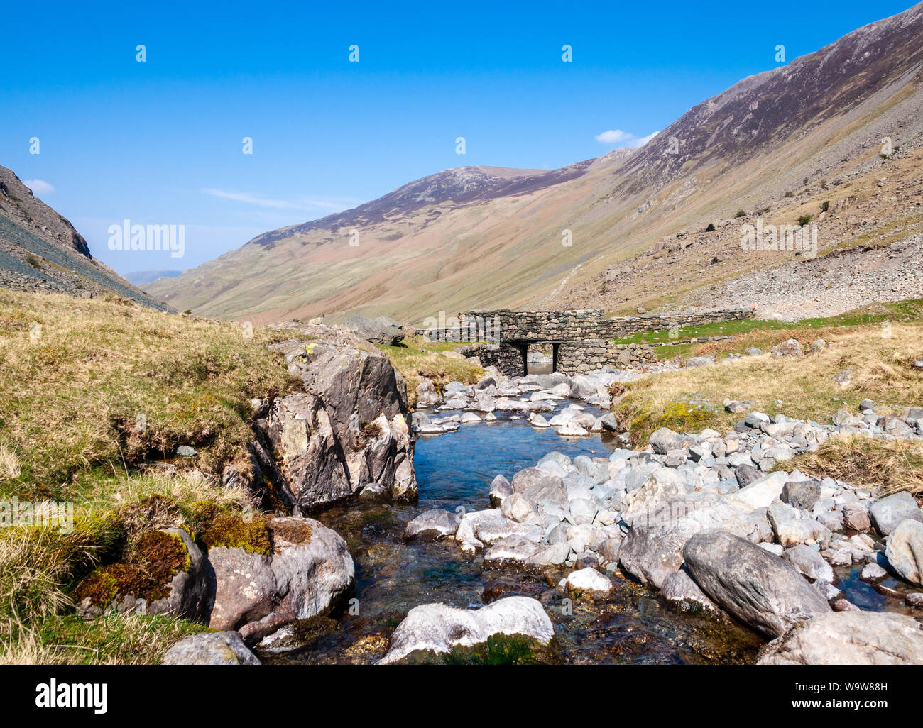 Le Gatesgarthdale Beck ruisseau de montagne coule sous un pont de pierre sur le Honister Pass road dans les montagnes de l'Angleterre de la Lake District. Banque D'Images