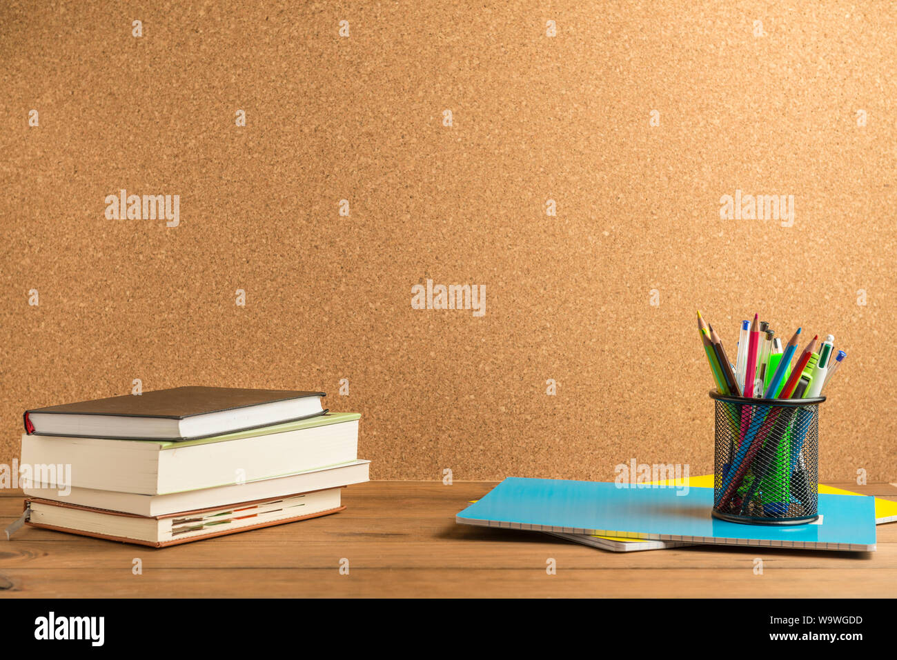 Livres, cahiers et un porte-crayons avec les crayons, stylos et fournitures scolaires diverses sur certains panneaux en bois avec un panneau de liège à l'arrière-plan. Banque D'Images