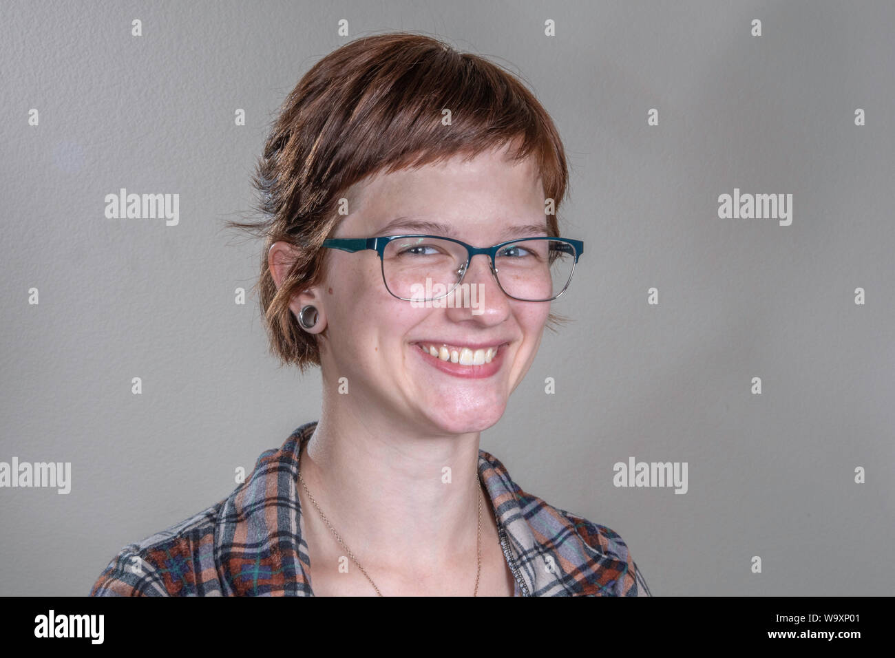 Une jolie jeune femme dans une chemise de flanelle occasionnels nous donne un sage, sourire, dans un tête-et-épaules studio shot. Banque D'Images