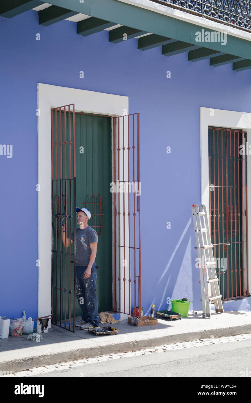 Peintre en bâtiment travaille sur la porte en fer volets avec tous ses outils portées par le mur peint en après-midi ensoleillé, le vieux San Juan, San Juan, Puerto Rico. Banque D'Images