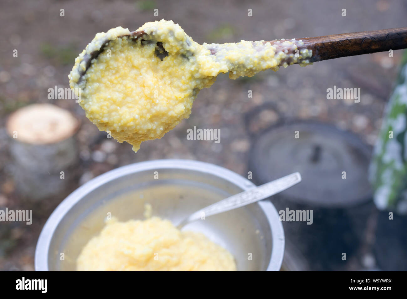 Grande cuillère en bois avec bouillie sur le fond de la cuisine du camp. Bouillie de maïs cuit à la jeu. camping. cuisine équipée pour les voyages Banque D'Images