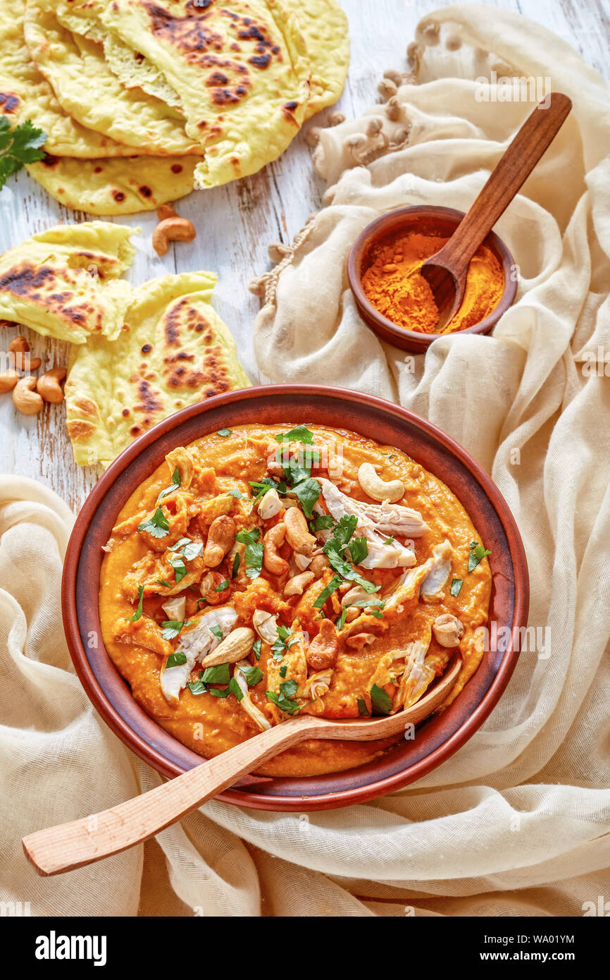 Soupe Mulligatawny épicé chaleureux avec la viande de poulet et le lait de coco saupoudré de cajou frits dans un bol avec chapati sur une table en bois blanc, un Indien Banque D'Images