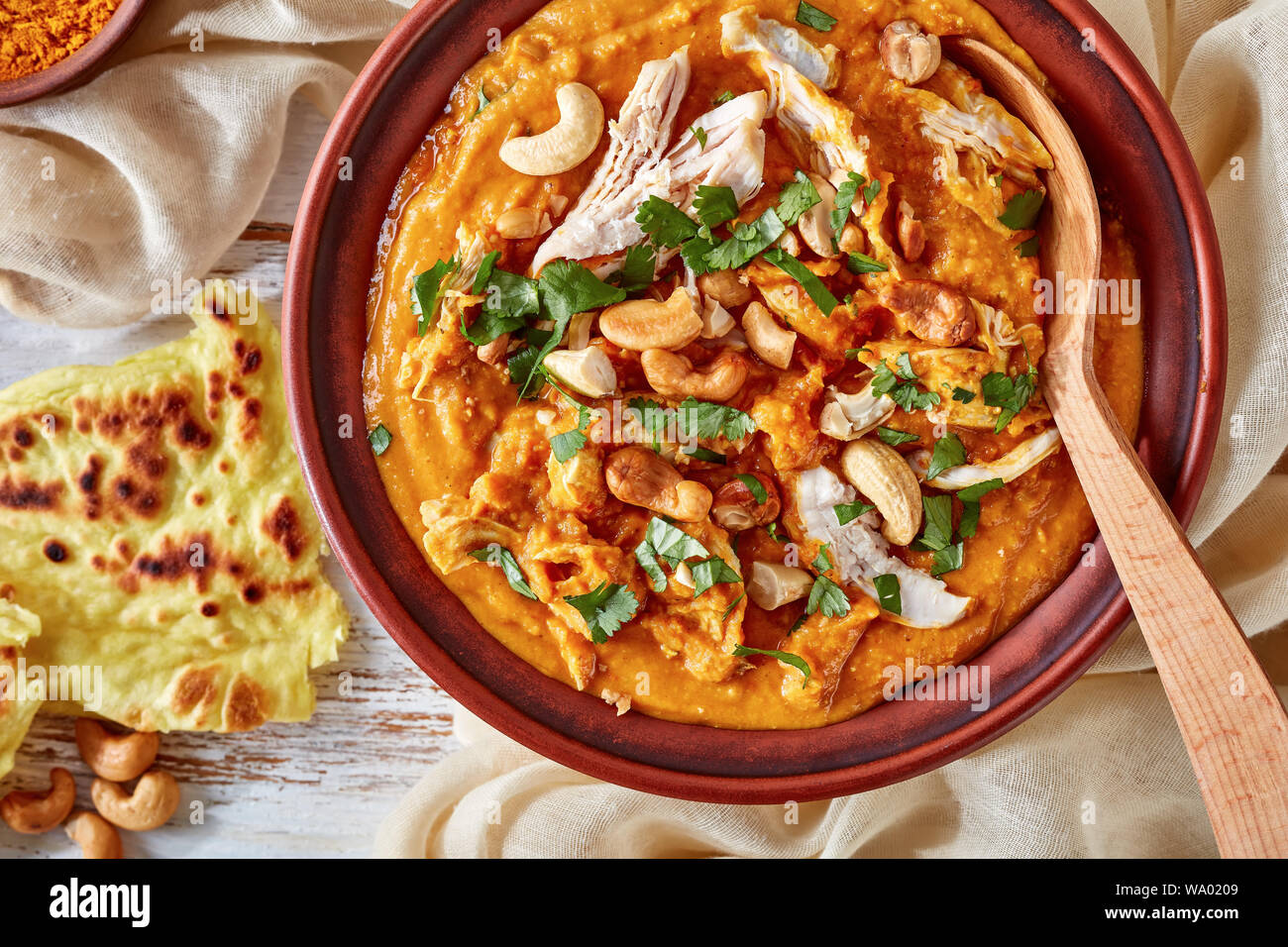 Soupe Mulligatawny épicé chaleureux avec la viande de poulet et le lait de coco saupoudré de cajou frits dans un bol avec chapati sur une table en bois blanc, un Indien Banque D'Images