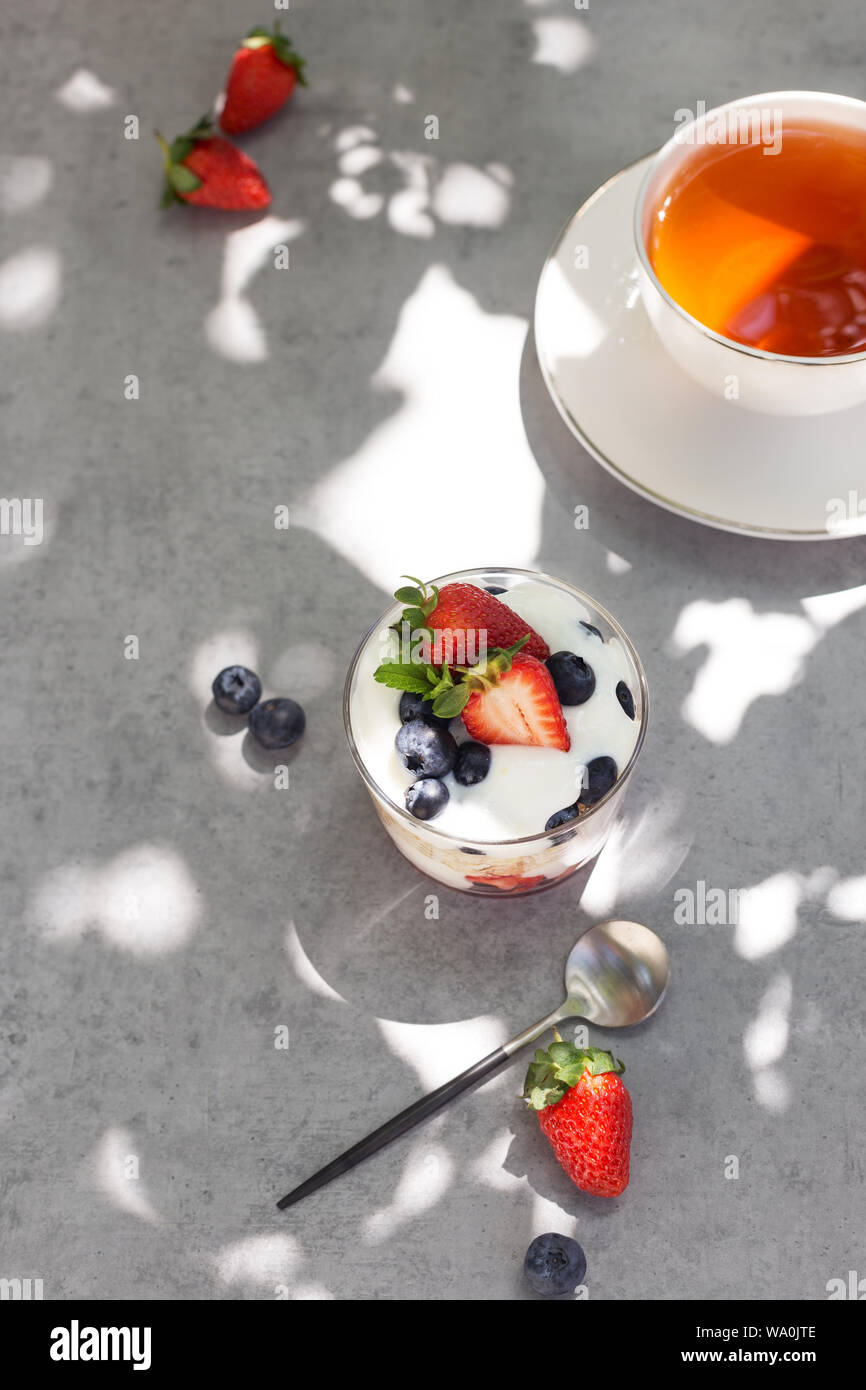 Vue de dessus avec granola yogourt en verre avec des petits fruits et une tasse de thé sur fond gris Banque D'Images Vue de dessus avec granola yogourt en verre avec des petits fruits et une tasse de thé sur fond gris Banque D'Images