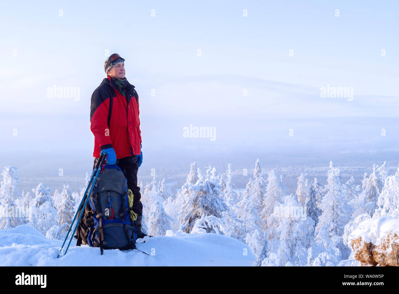 Meilleur homme debout dans un paysage d'hiver glacial près de son sac à dos sur une falaise et regarde dans la distance Banque D'Images