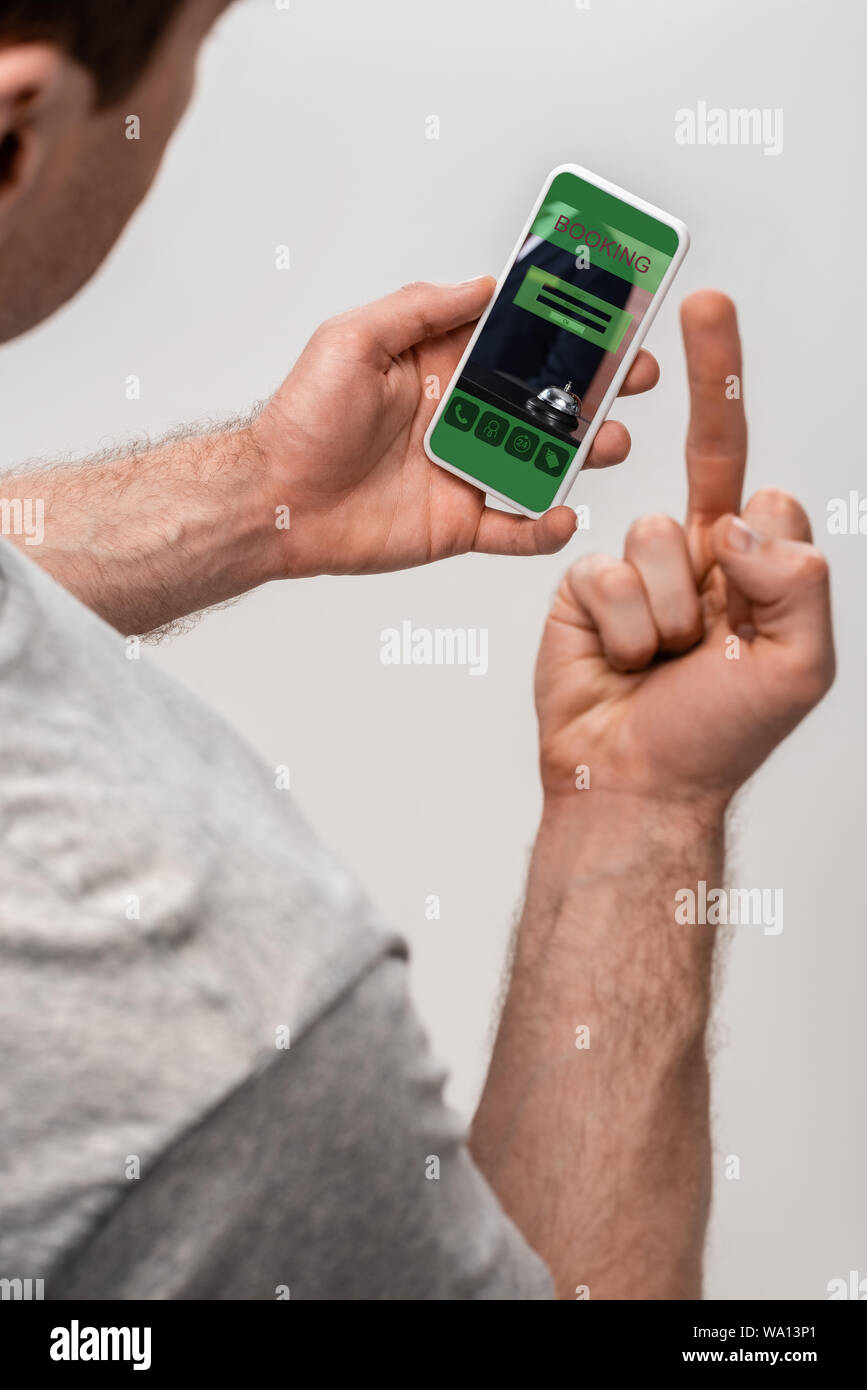 Portrait de l'homme en utilisant smartphone avec l'application de réservation et montrant le majeur, isolé sur gris Banque D'Images