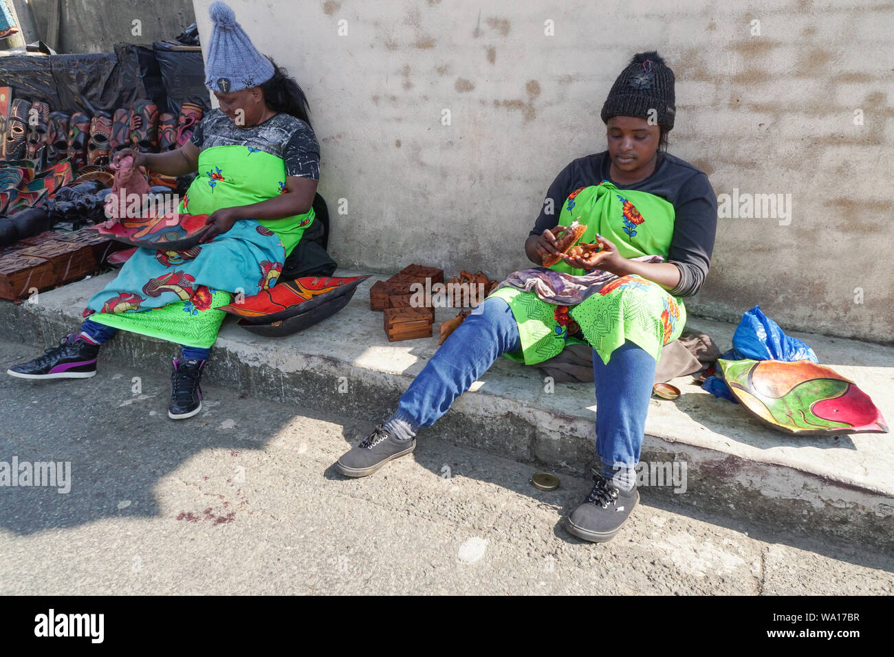 Deux femmes noires africaines ou les femmes vendeuses de rue travail assis sur des produits ou articles en bois à l'extérieur de leurs stalles dans dieux,fenêtre Mpumalanga, Afrique du Sud Banque D'Images