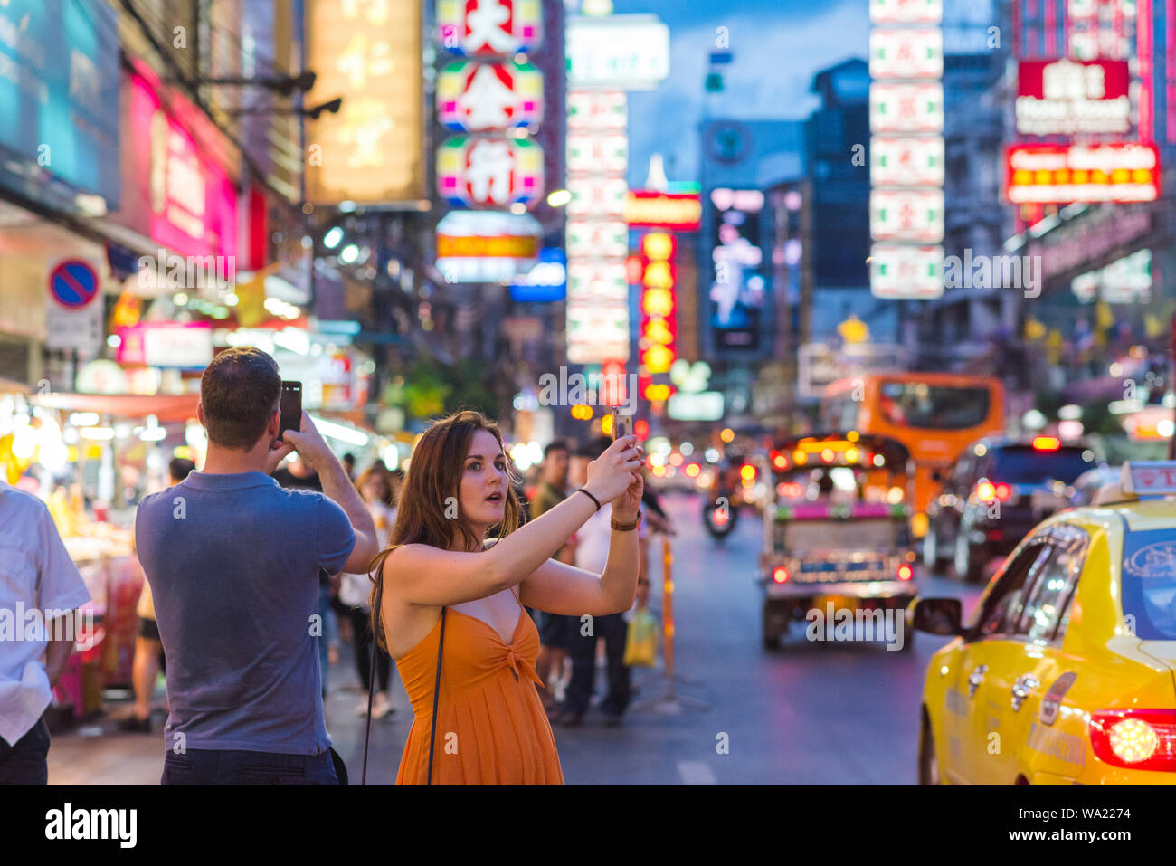 Bangkok, Thaïlande : 2 touristes admiratifs, qui vient d'arriver en taxi, tirer avec leur téléphone mobile nuit beauté de Yaowarat Road, Chinatown de nuit. Banque D'Images