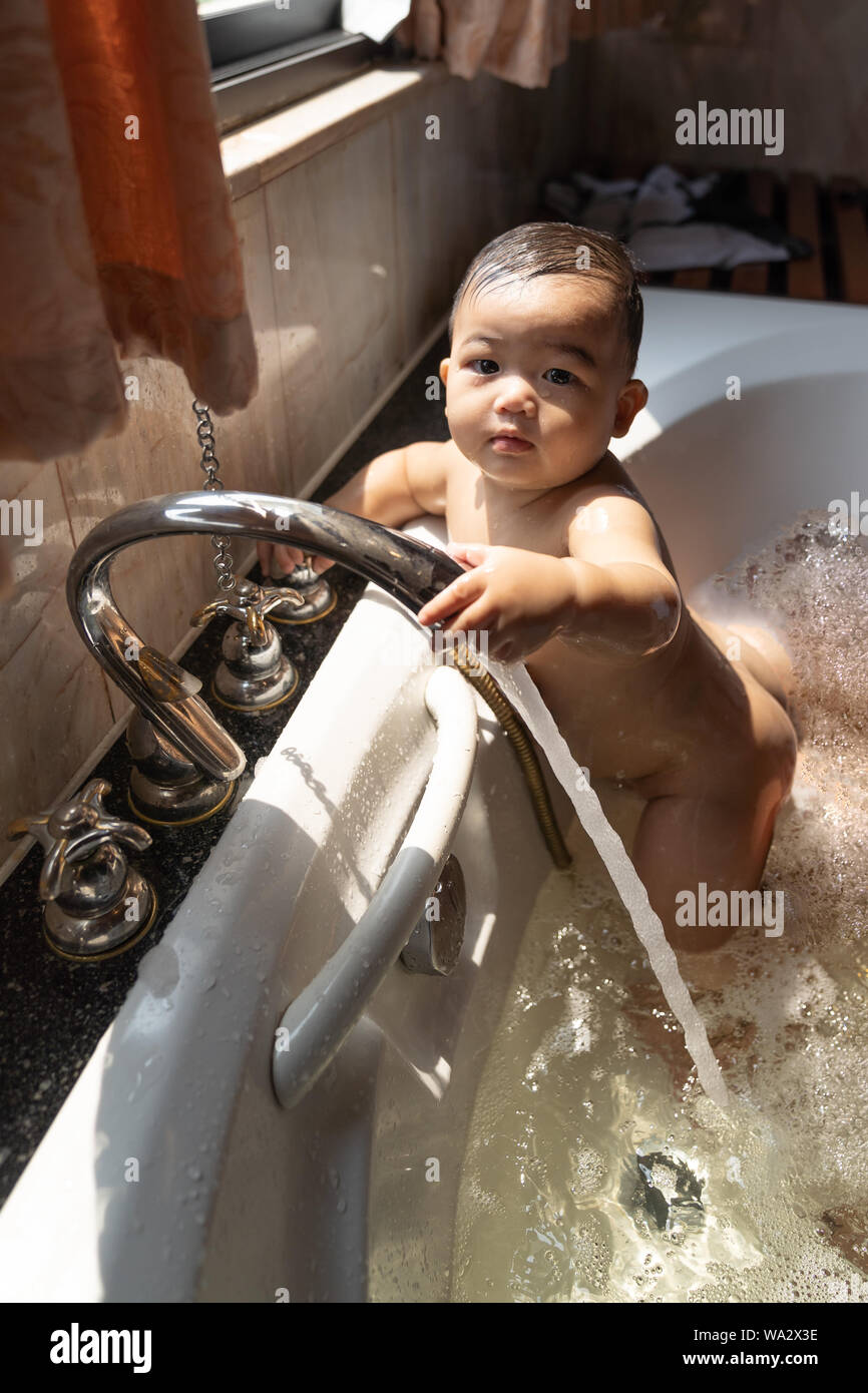 Happy laughing baby boy asiatique prenant un bain en jouant avec des bulles de mousse. Petit enfant dans une baignoire. Smiling chevreau dans salle de bains avec fenêtre soleil background Banque D'Images