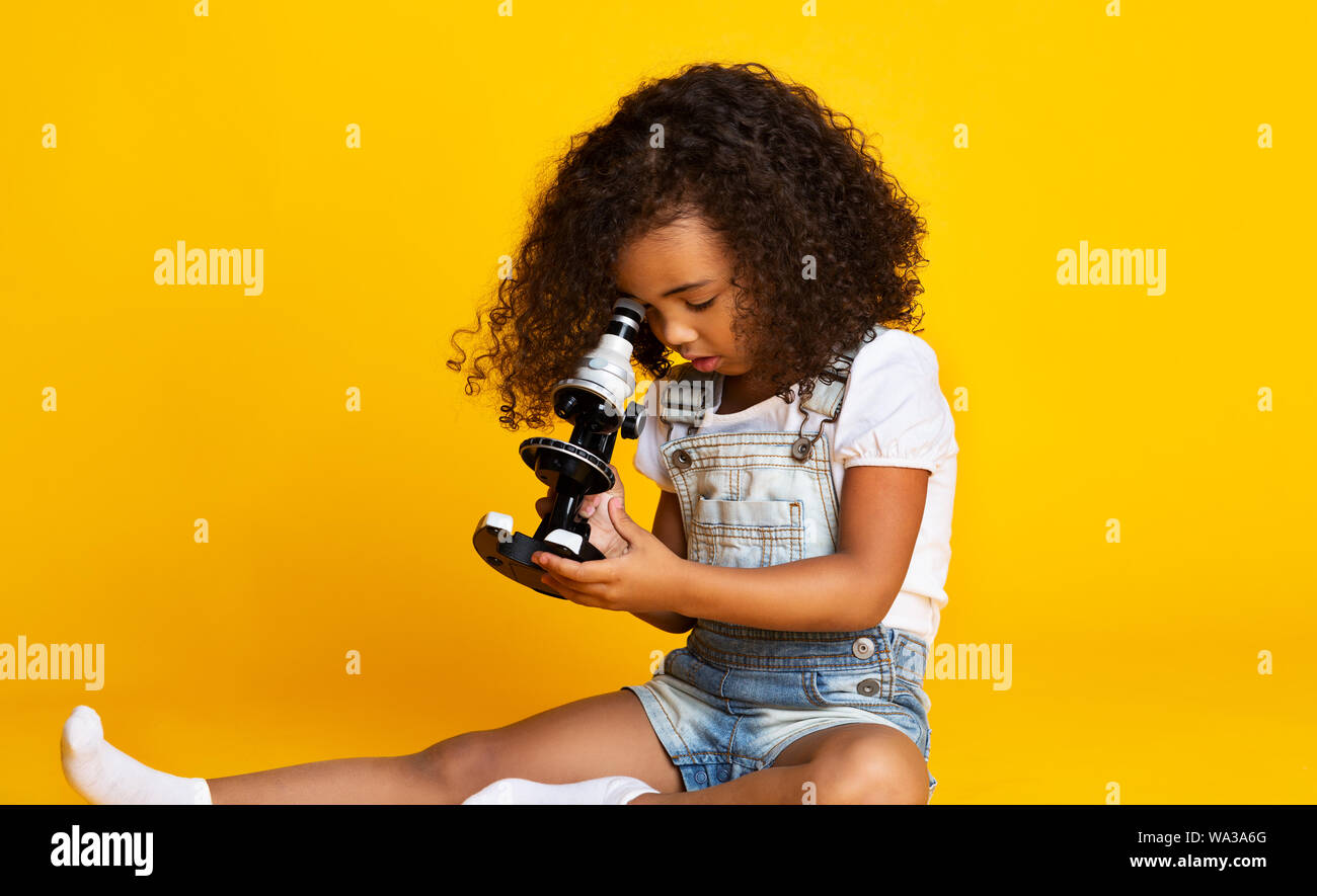 Peu d'afro girl looking through microscope, fond jaune Banque D'Images