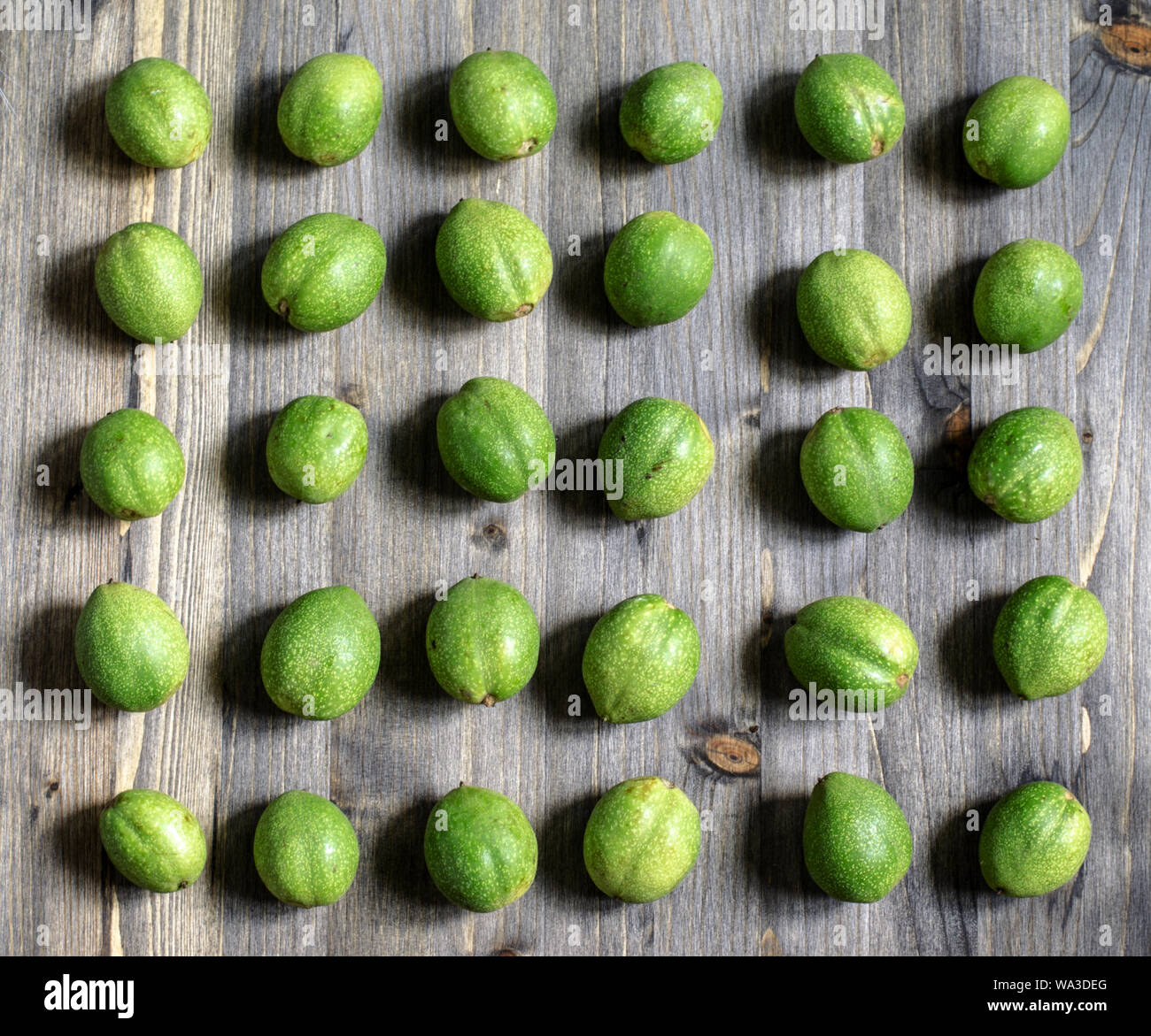Les jeunes fruits verts de noix se trouvent dans les rangées sur un fond de bois gris. Banque D'Images