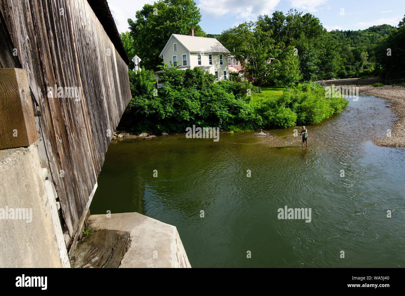 Sur un pont couvert en face de lui, un pêcheur de mouche jette sa ligne sur la rivière Mad à Waitsfield, Vermont. Banque D'Images