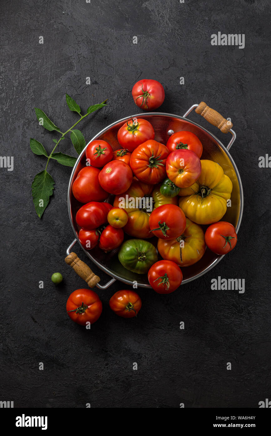 Tomates mûres dans une casserole sur fond noir en noir, exemplaire de l'espace. Banque D'Images