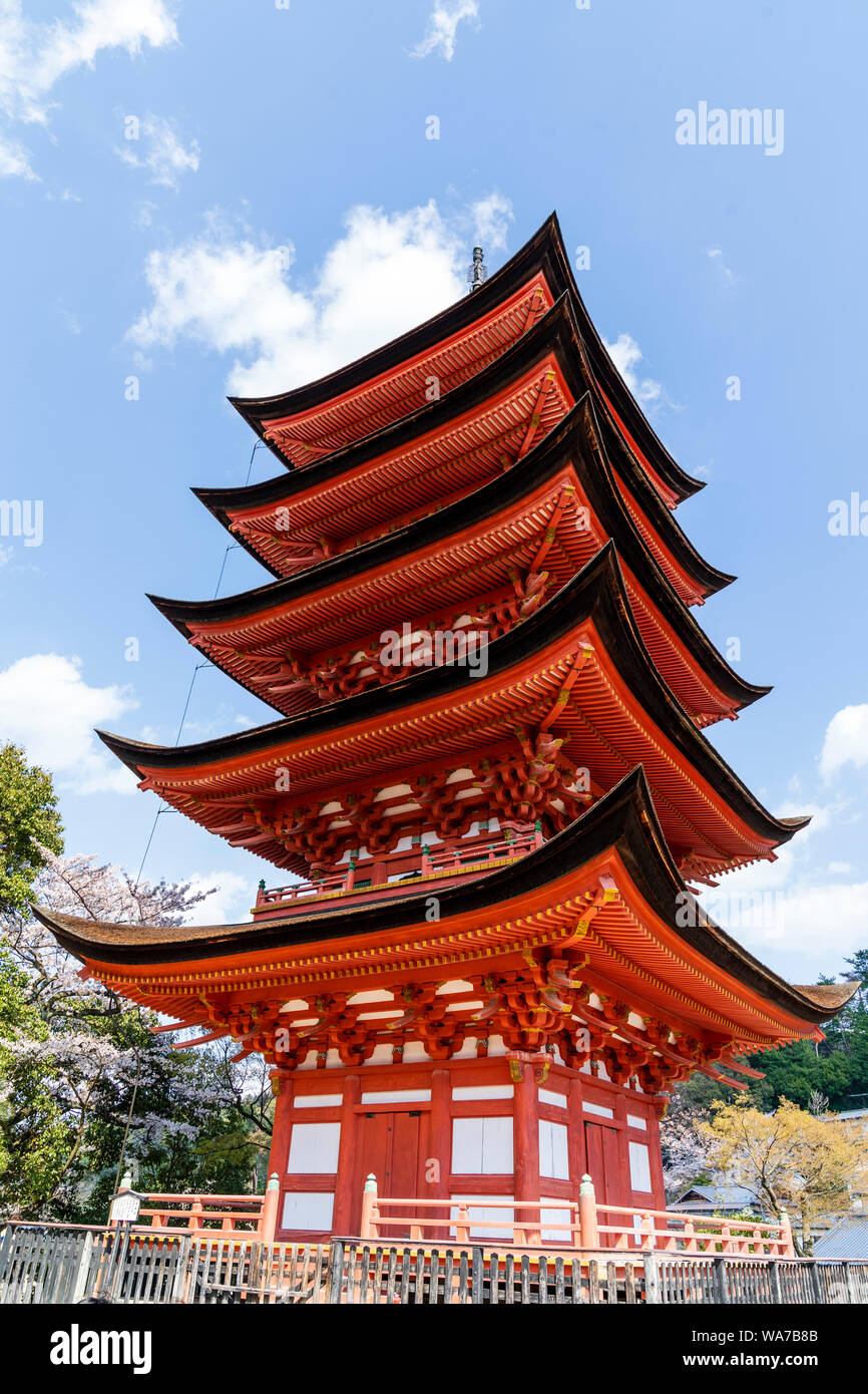 Le Japon, l'île de Miyajima. Le rouge de style japonais, la pagode de cinq étages, avec Gojunoto cerisiers au premier plan, et le ciel bleu derrière. Banque D'Images
