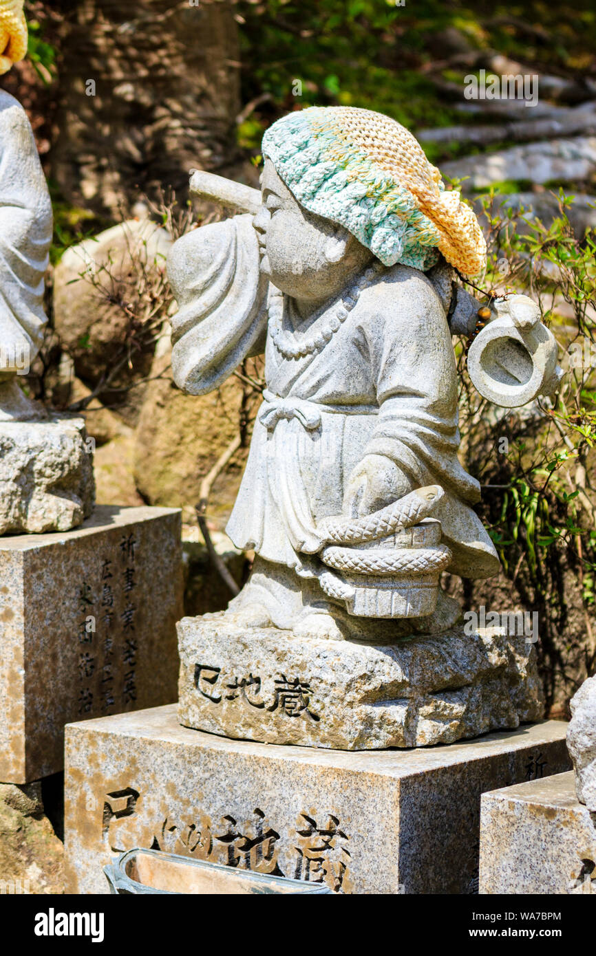 Le Japon, Miyajima. Daisho-in temple. Petite statue Jizo de pierre d'un moine bouddhiste debout portant un serpent enroulé autour de la benne avec porte et bonnet de laine. Banque D'Images