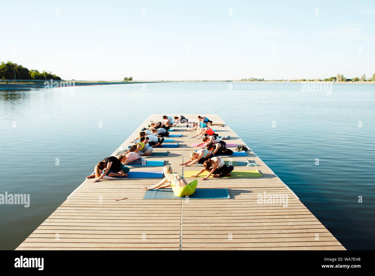 Un grand groupe de personnes qui assistent à des cours de yoga sur un ponton près du lac. Activités de plein air d'été Banque D'Images