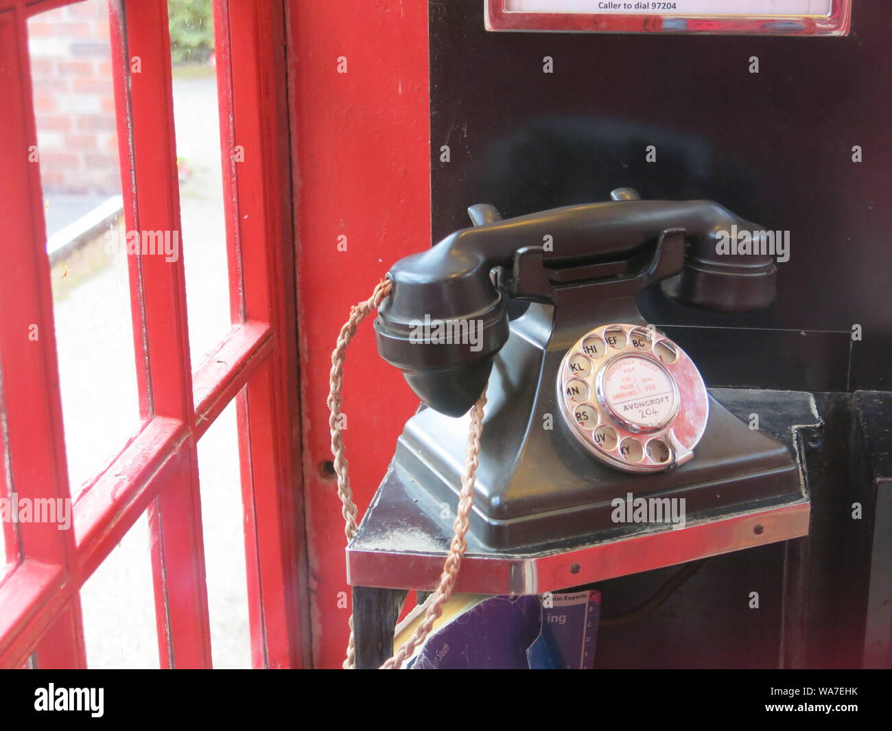 Close-up d'un vieux téléphone noir lourd avec le cadran circulaire pour la numérotation des doigts, dans un téléphone public fort rouge. Banque D'Images