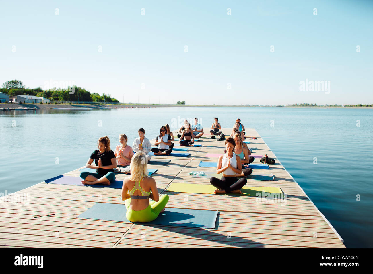 Un grand groupe de personnes qui assistent à des cours de yoga sur un ponton près du lac. Activités de plein air d'été Banque D'Images