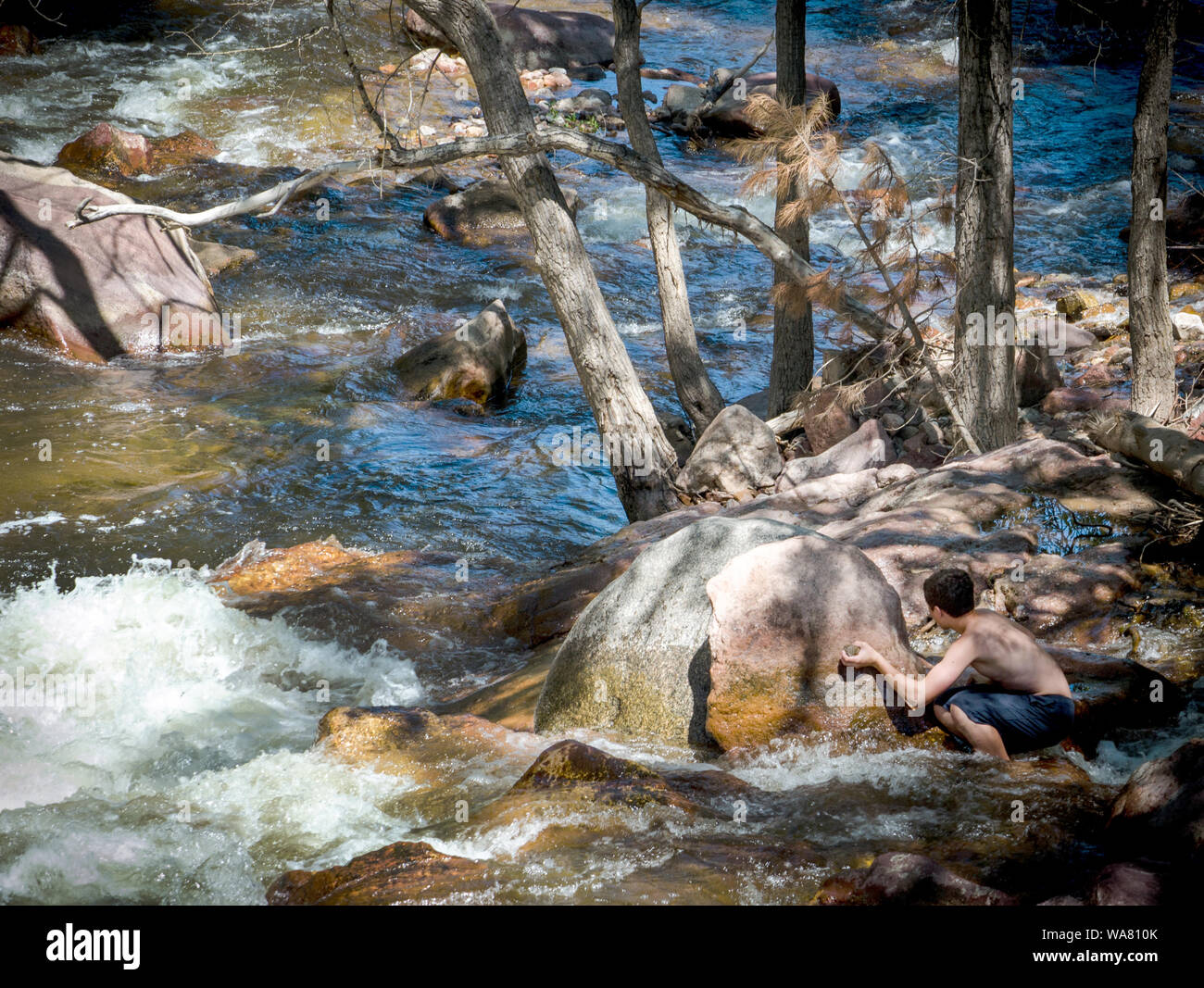 Un jeune adolescent se cache derrière un gros rocher, à Boulder Creek dans le Colorado aux États-Unis. Banque D'Images