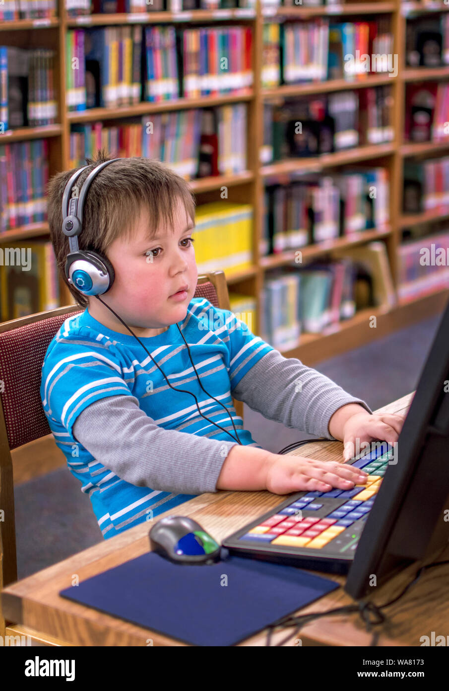 Un petit garçon portant des écouteurs, joue sur un ordinateur portable à la bibliothèque publique locale Banque D'Images