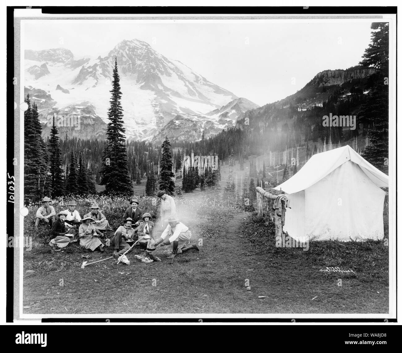 Camping partie d'hommes et de femmes de la cuisson à feu de camp et manger près de tente à Henry, Mt. Rainier National Park, Washington] / Curtis & Miller Banque D'Images